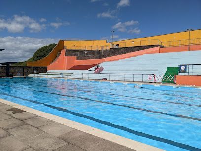 Outdoor swimming pool with bleachers under a blue sky.