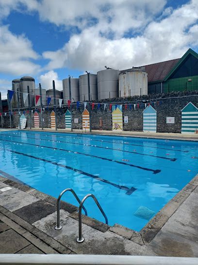 Outdoor swimming pool with blue water, colorful changing huts, and cloudy sky.