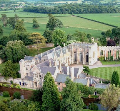 Aerial view of a large, light-colored stone building surrounded by green fields and trees.