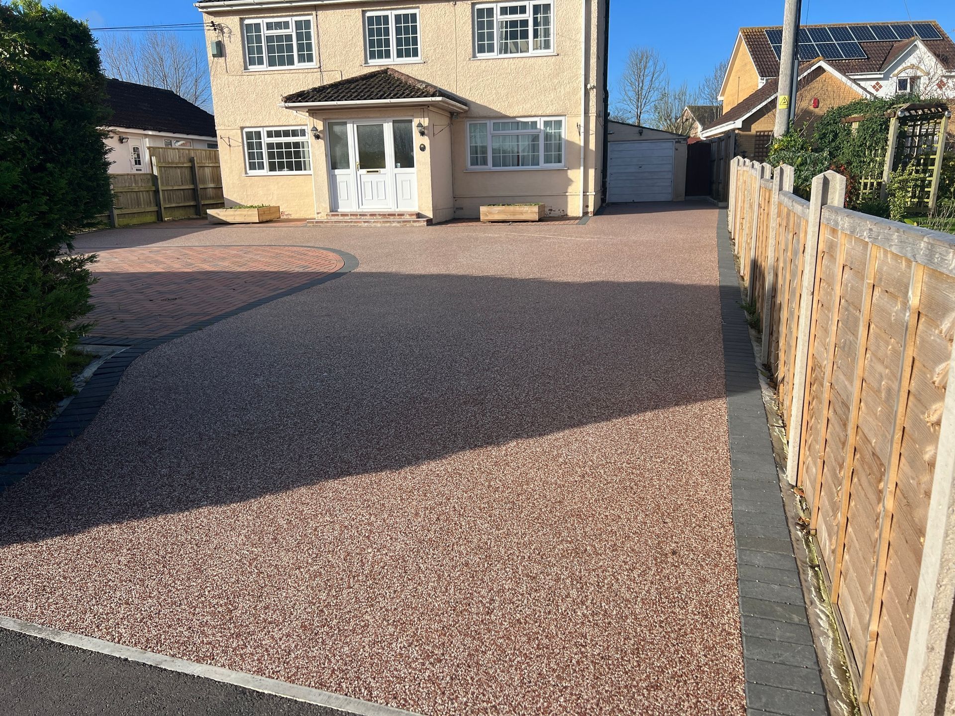 Gravel driveway in front of a two-story house with a wooden fence on the right.