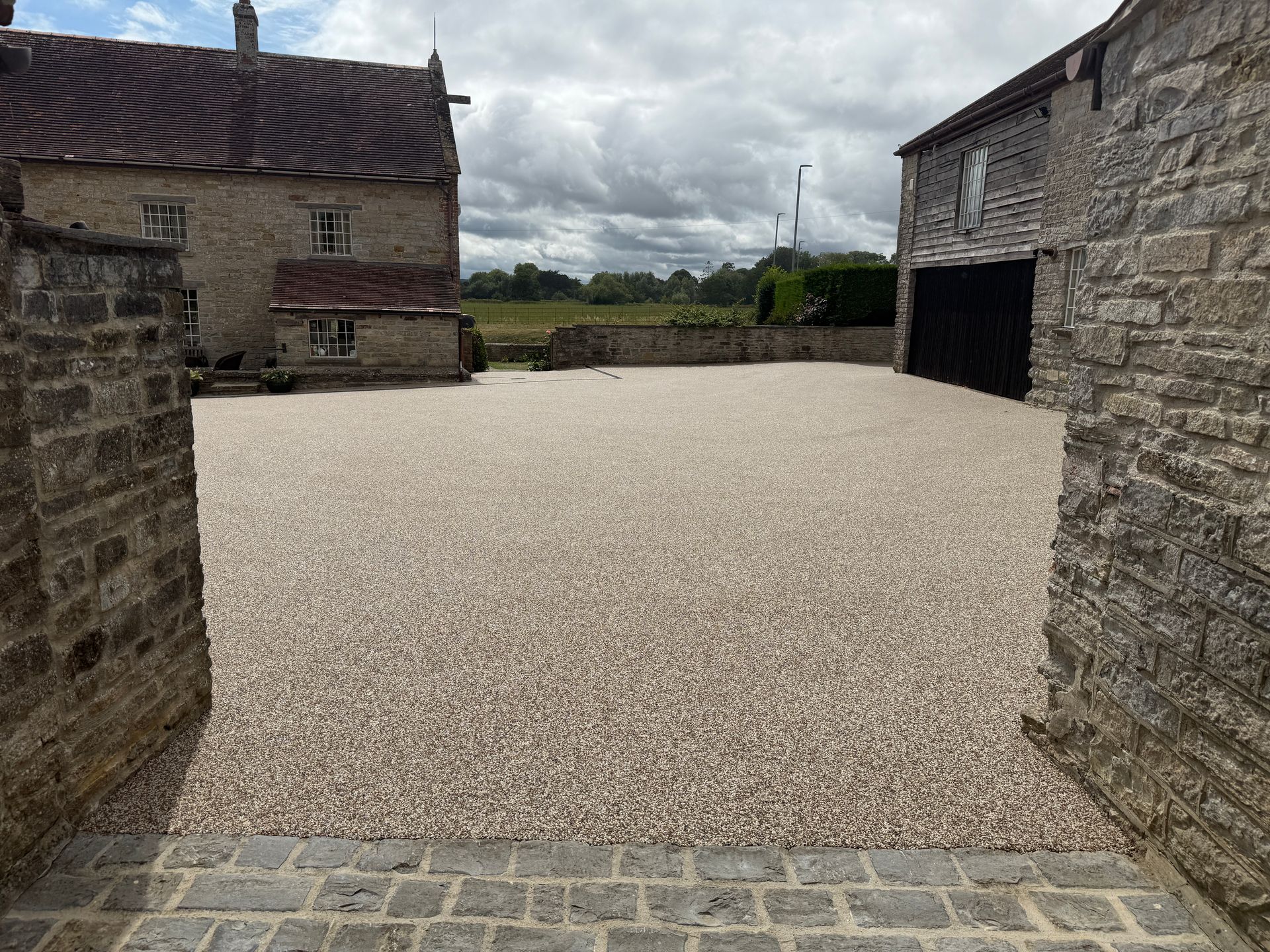 Gravel driveway between stone buildings under cloudy sky.