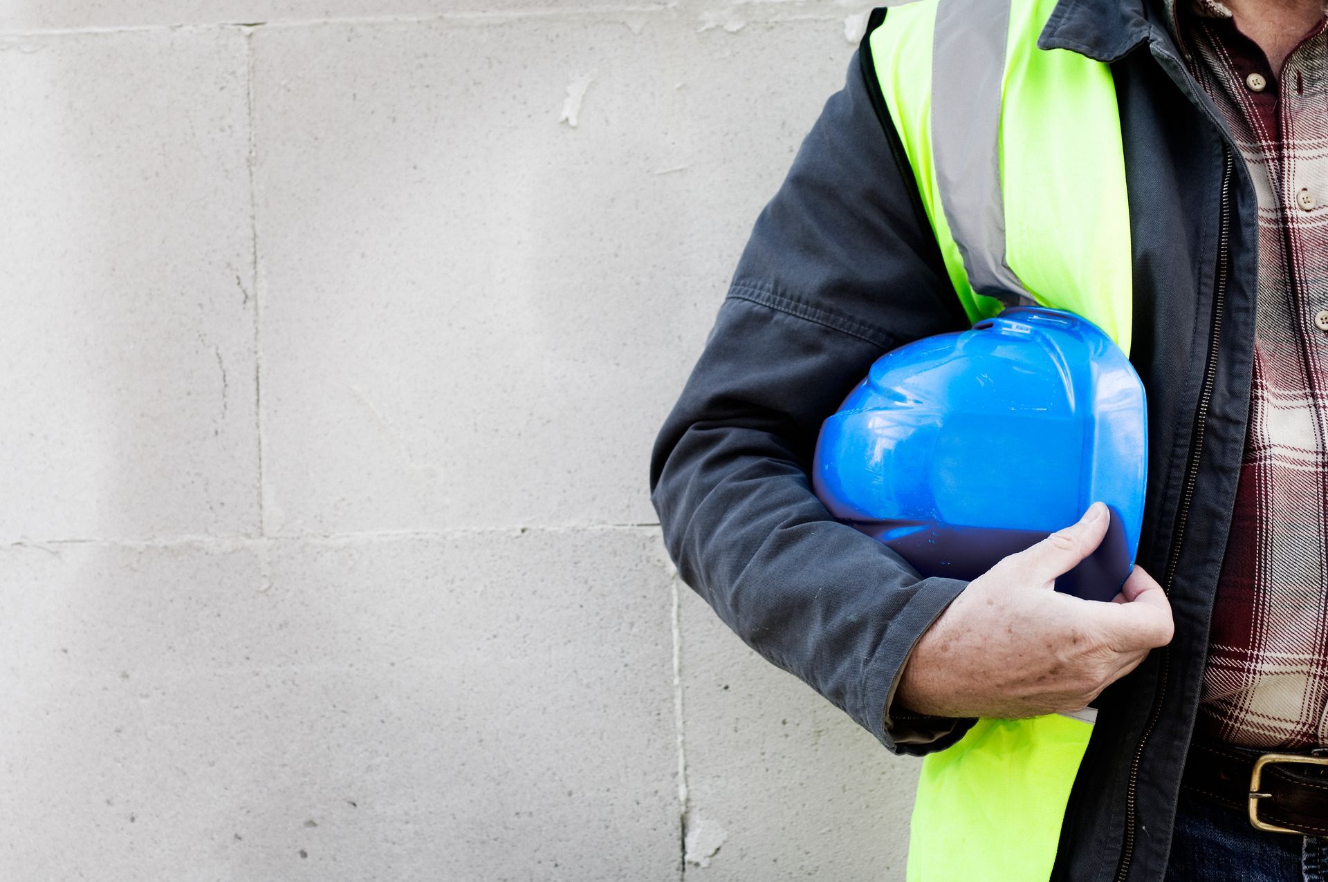 Un uomo che indossa un giubbotto giallo tiene in mano un casco blu.