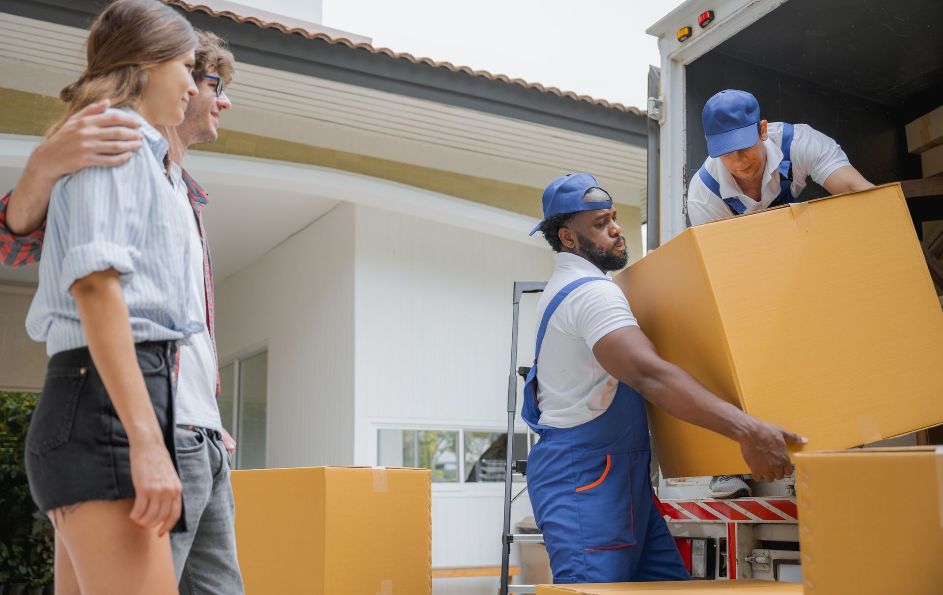 Moving crew loading boxes into truck; couple watches.
