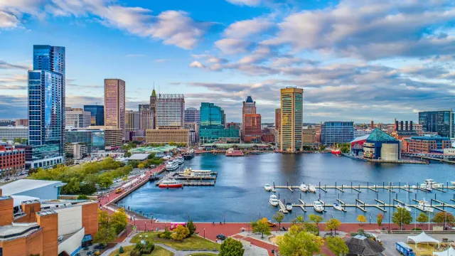 City skyline across a harbor with boats, modern buildings, and a cloudy blue sky