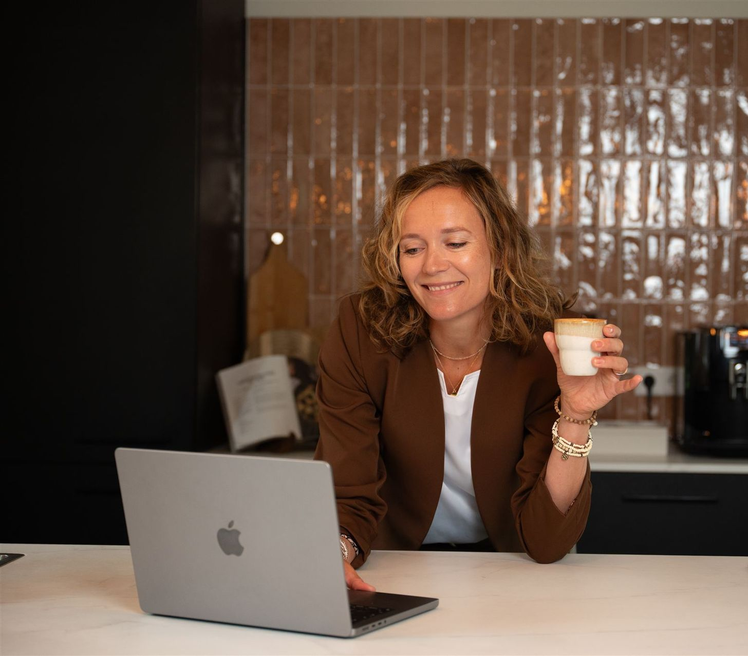 Zittend achter laptop met kop koffie, lachend en geconcentreerd, beeld van werkplezier en productiviteit