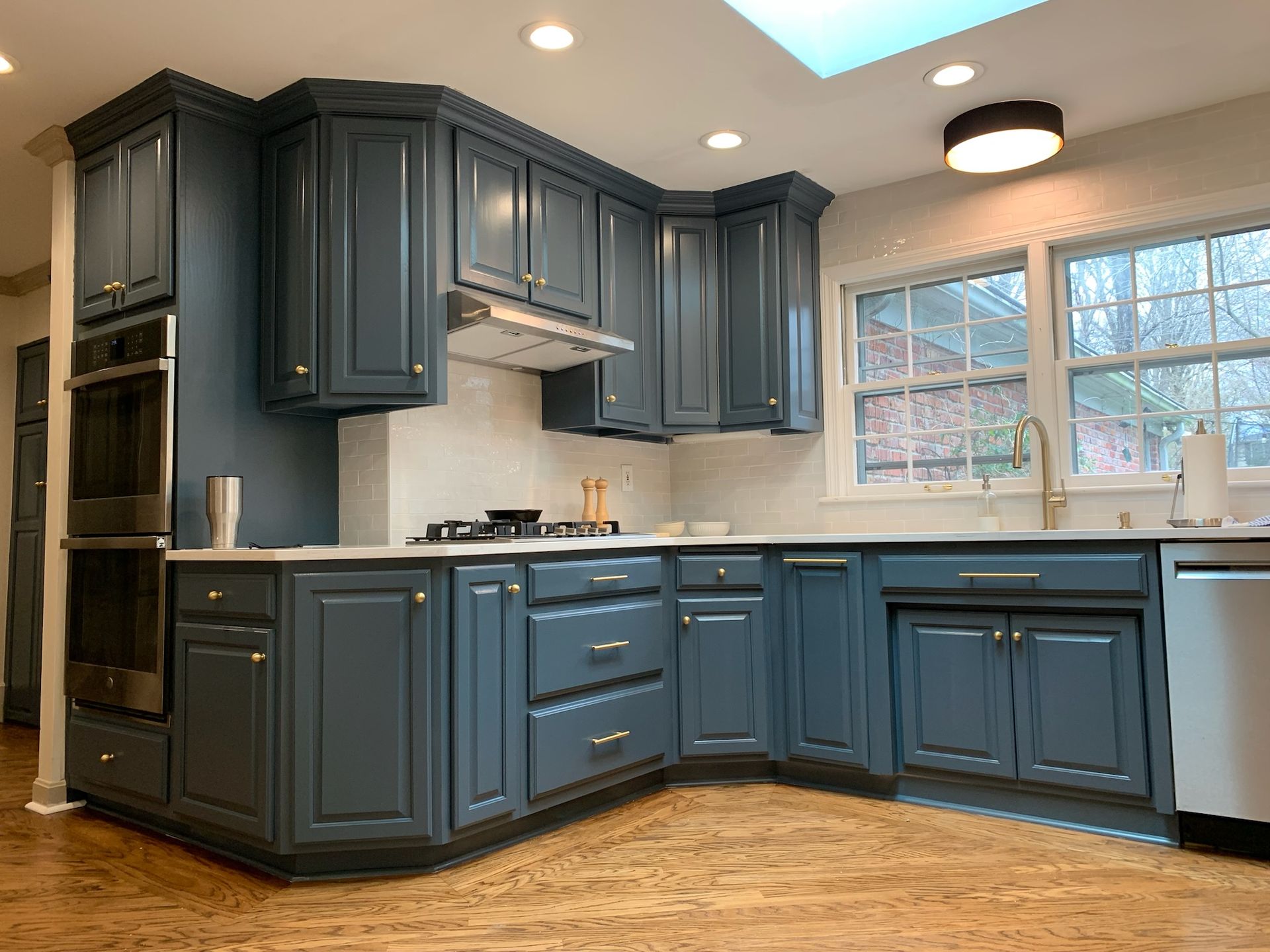 Blue kitchen cabinets with white countertops, stainless steel appliances, and wooden floors.