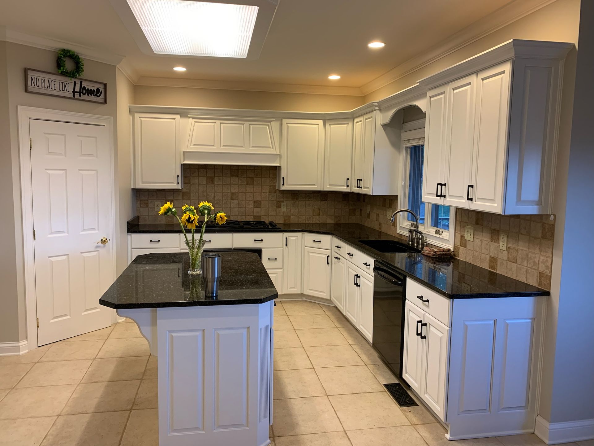 A kitchen with white cabinets , black counter tops , and a large island.