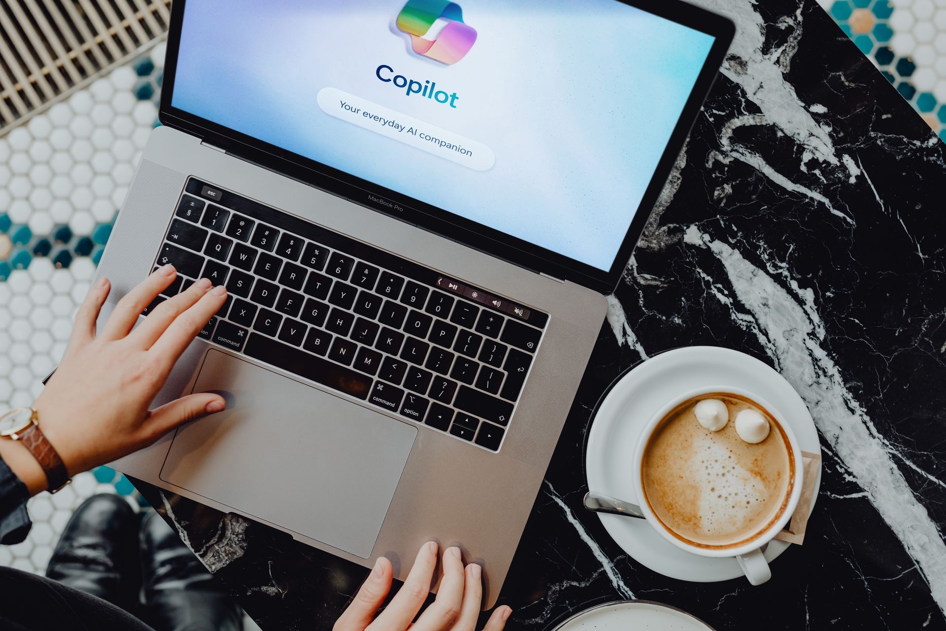 Hands typing on a laptop next to a coffee cup on a black marble desk