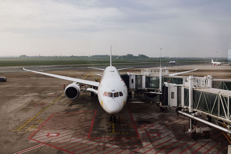 Airplane parked at an airport gate with a jet bridge on the right under a cloudy sky
