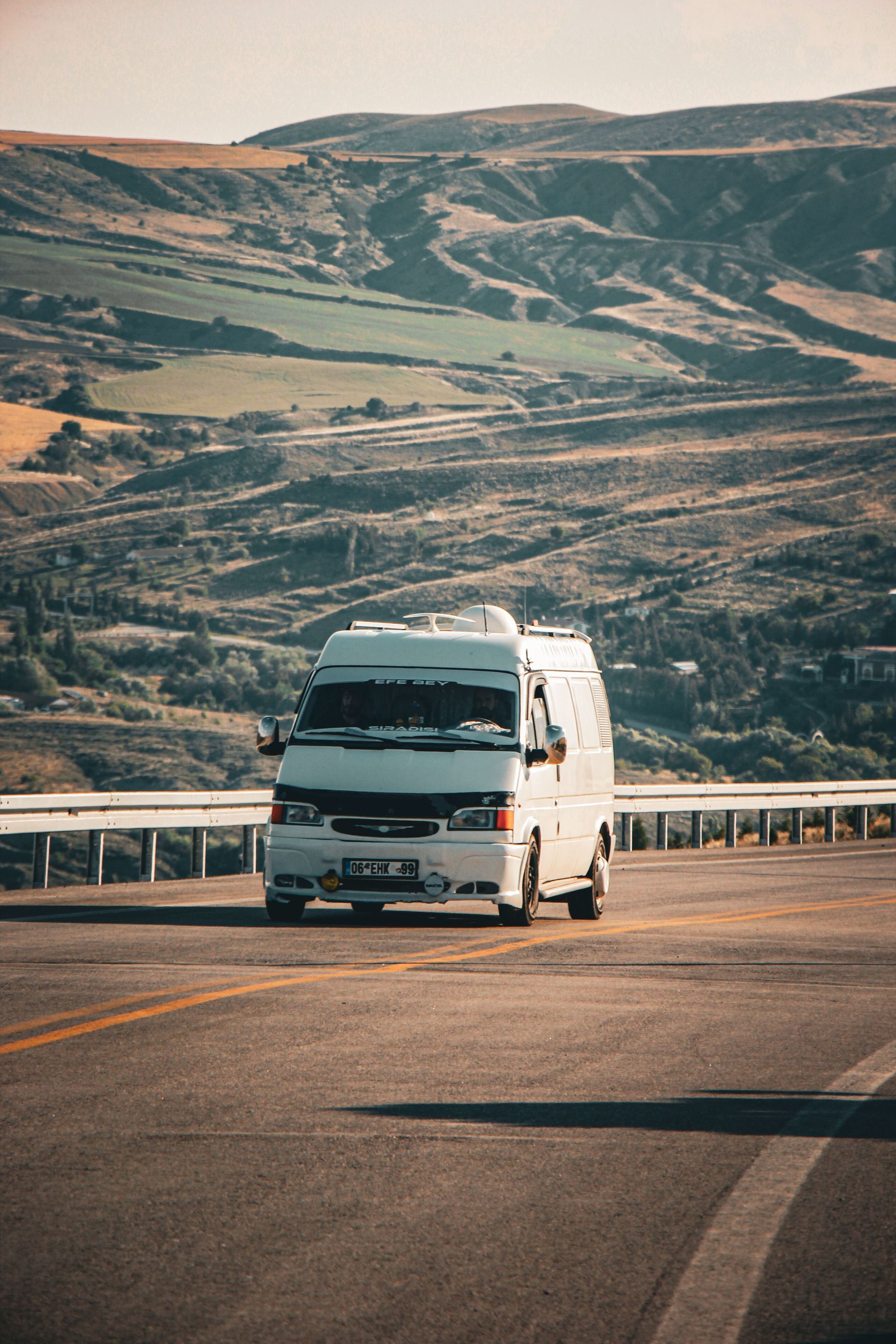 White camper van driving on a road through hilly countryside