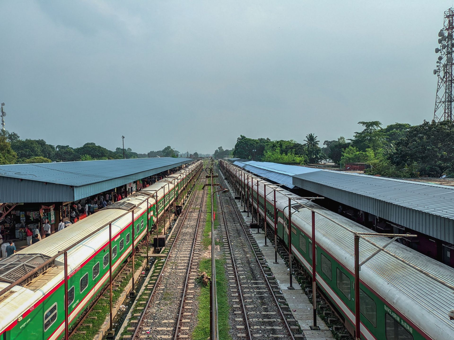 Train platforms with green-and-white trains on both sides of a central track under a cloudy sky