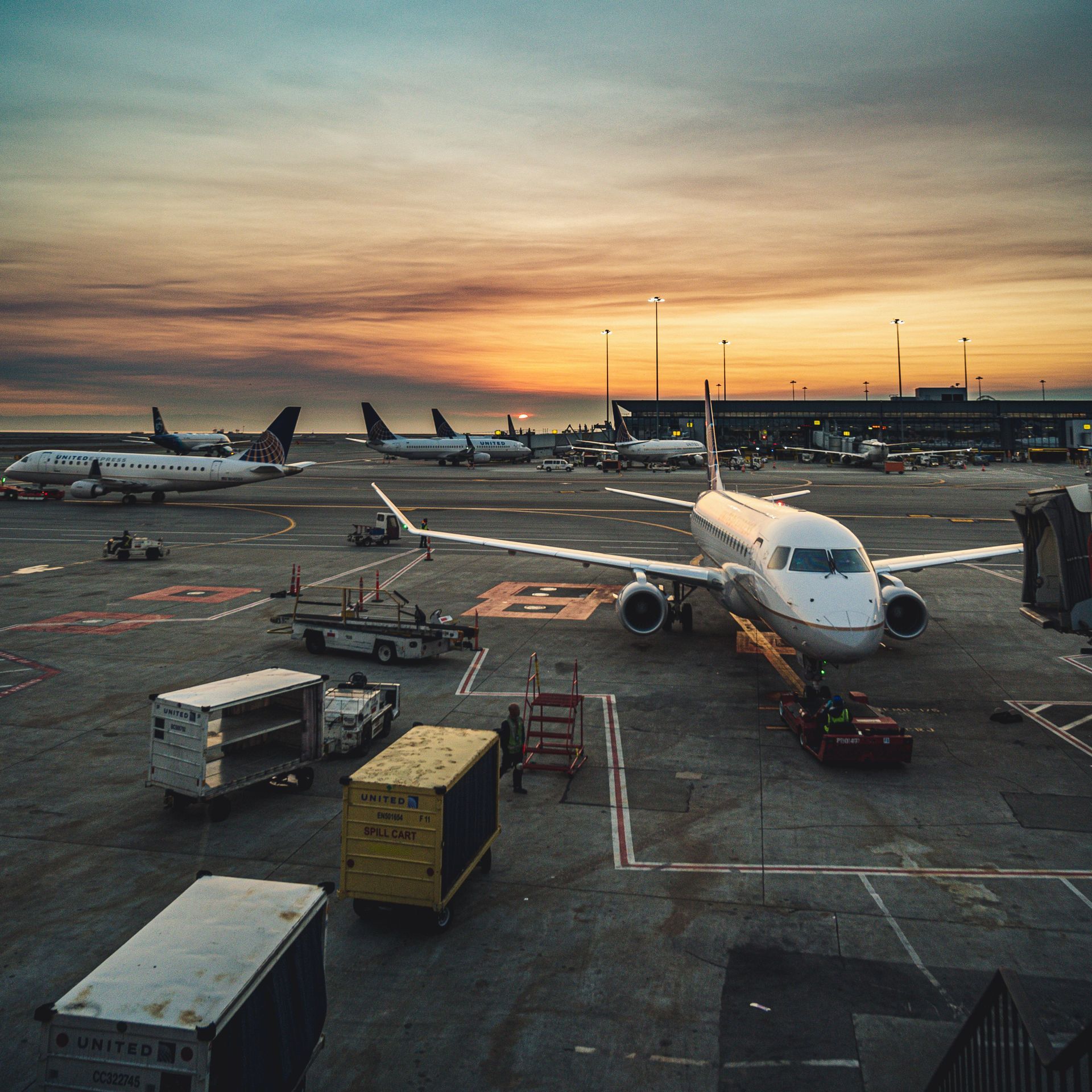 Airplane parked at airport gate at sunset, with ground vehicles and other jets in the background