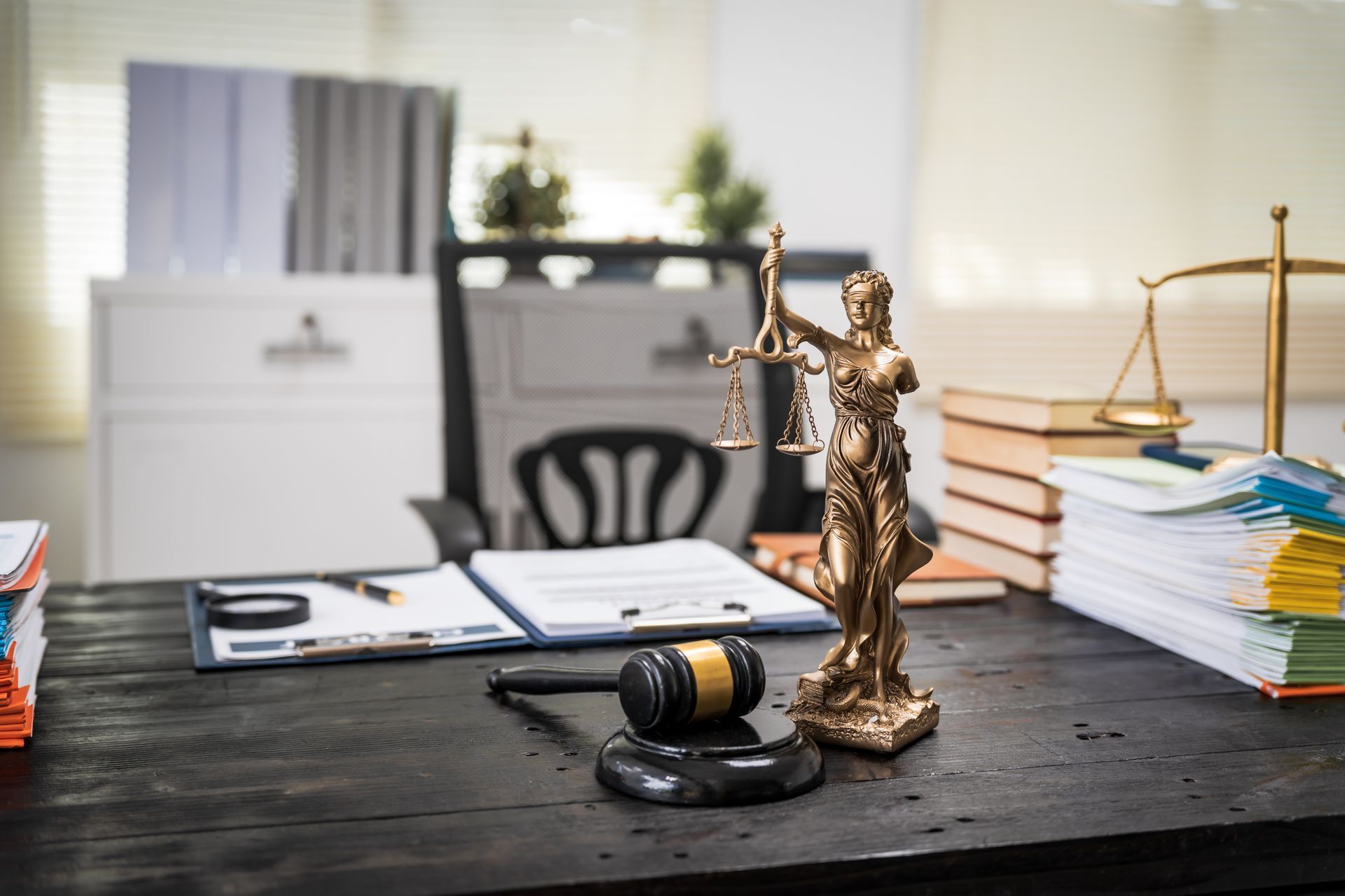 Lady Justice statue and gavel on a desk with legal documents and stacked files.