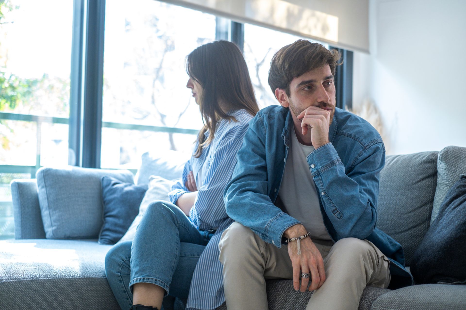 Two people sitting apart on a couch, looking away in a tense living room.