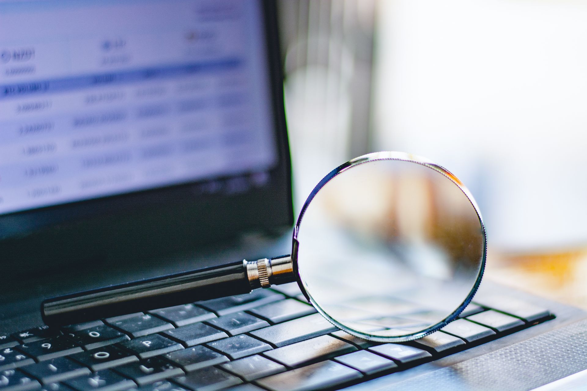 Magnifying glass on a laptop keyboard with a blurred computer screen in the background