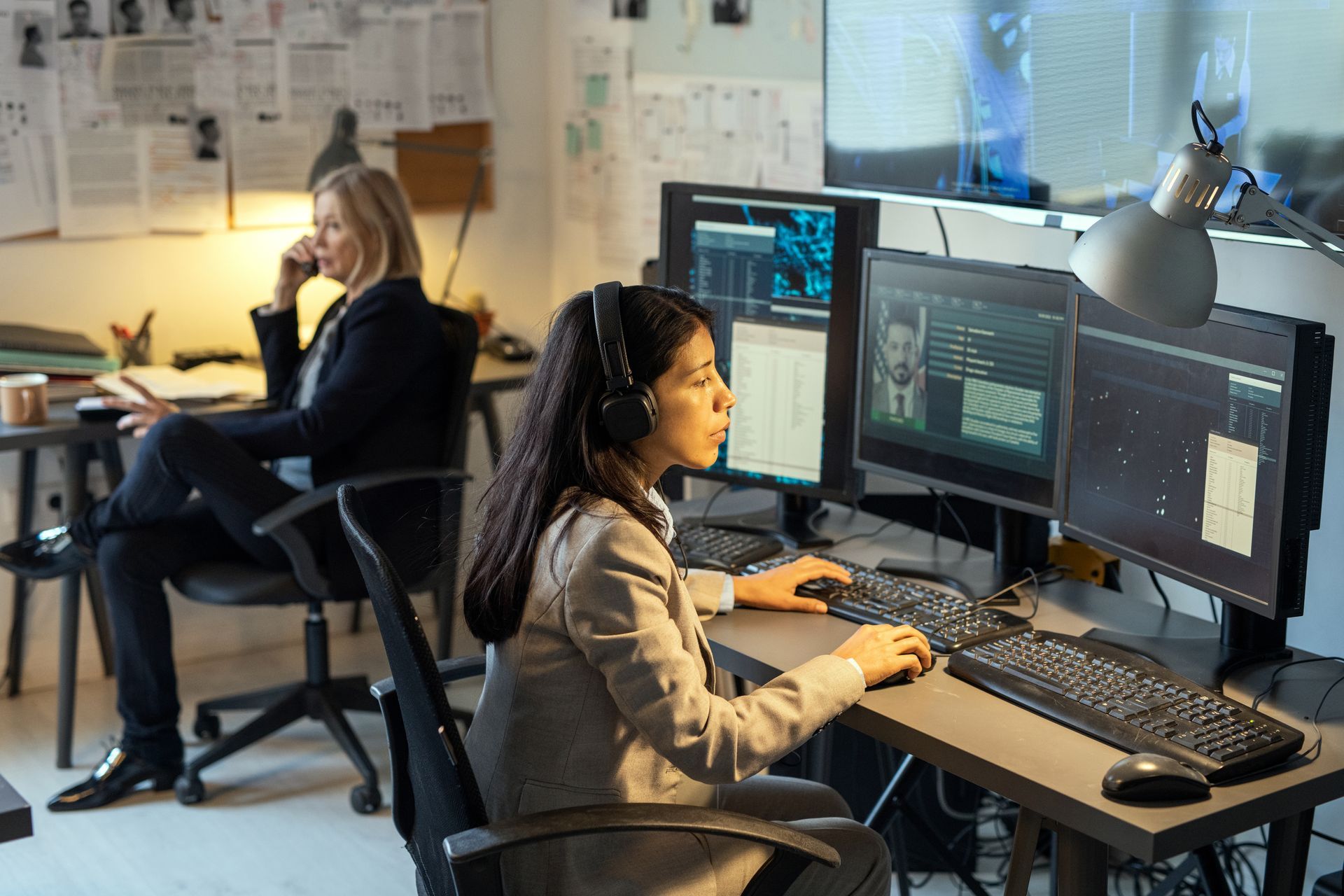 One agent sitting in front of computer monitors and another detective talking on a phone. One agent sitting in front of computer monitors and another detective talking on a phone.