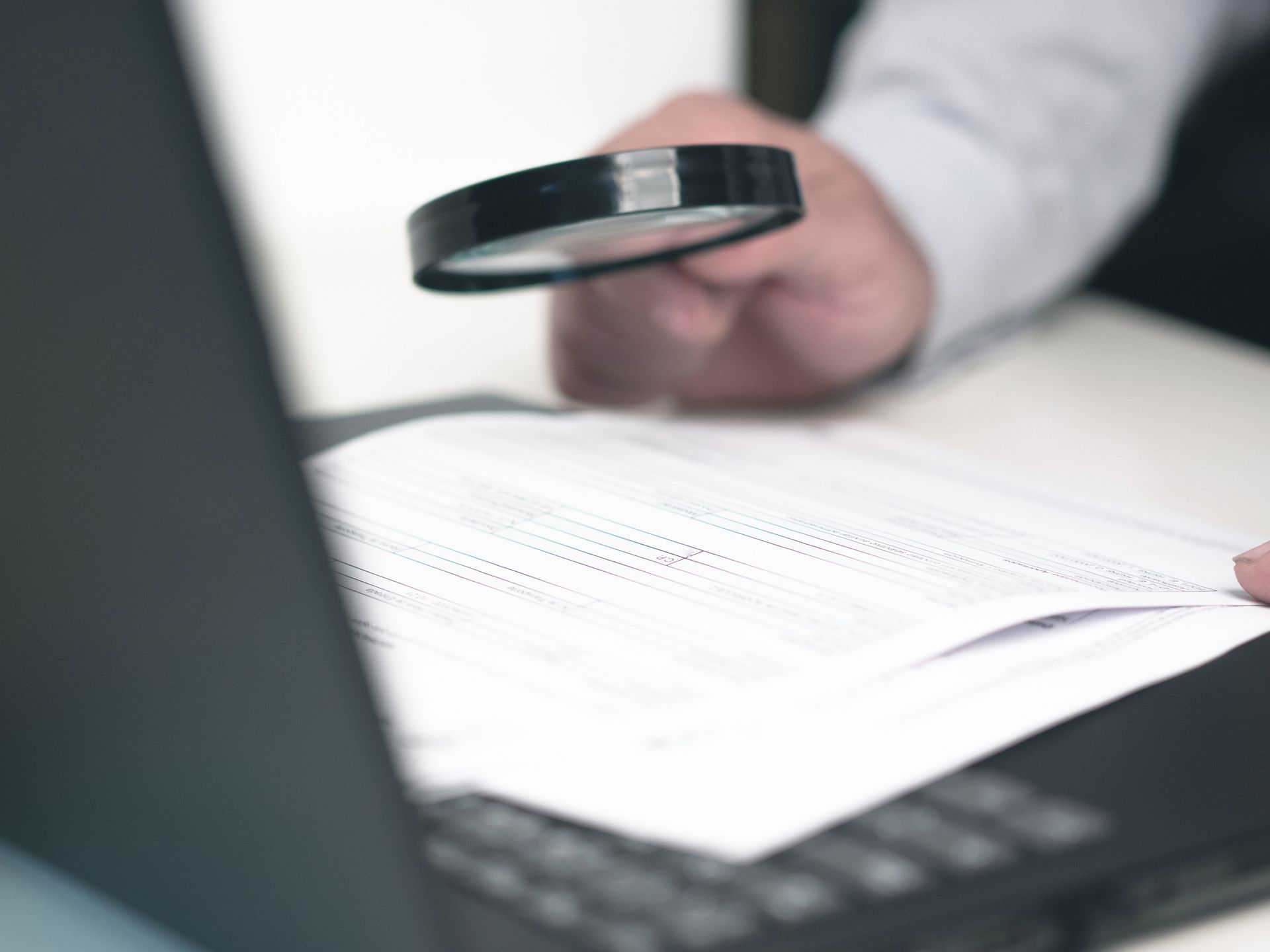 Close-up of a magnifying glass being held by a hand while poring over a document.