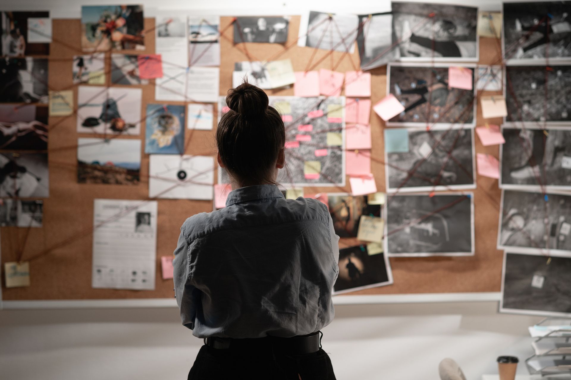 A back view of a female detective looking attentively at an investigation board