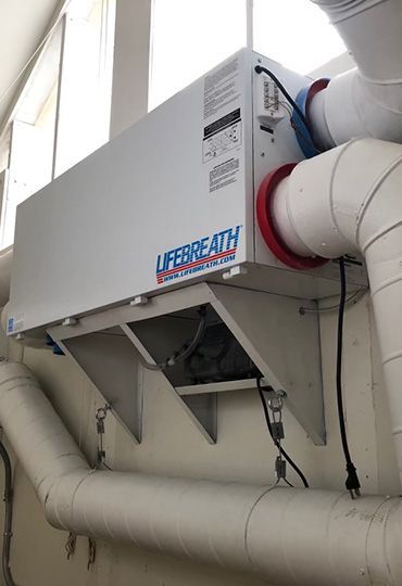 Large white industrial HVAC unit with ductwork mounted near a ceiling indoors