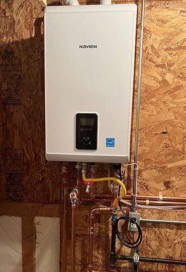 White wall-mounted water heater with pipes in an unfinished room with exposed plywood walls.