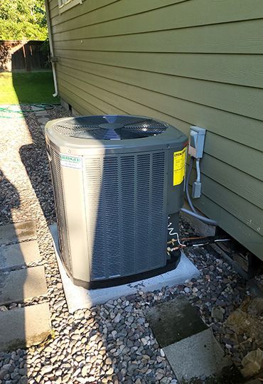 Outdoor air conditioning unit beside a house wall on a gravel path