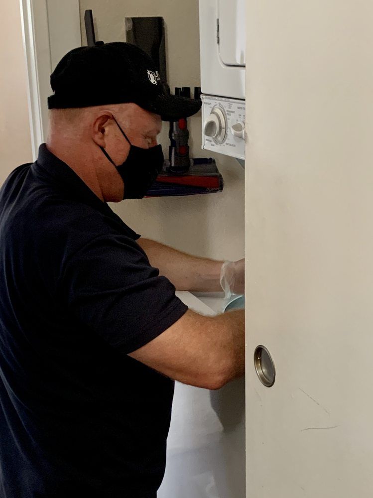 A man wearing a mask and gloves is working on a washer and dryer.