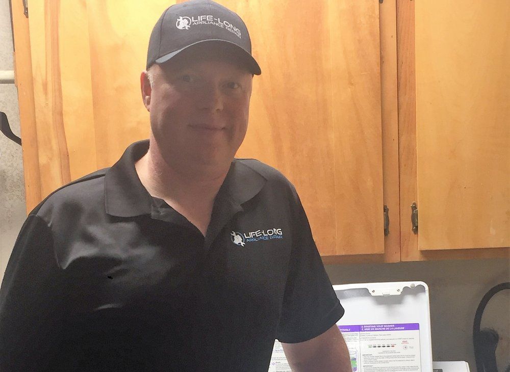 A man wearing a hat and a black shirt is standing in a kitchen.
