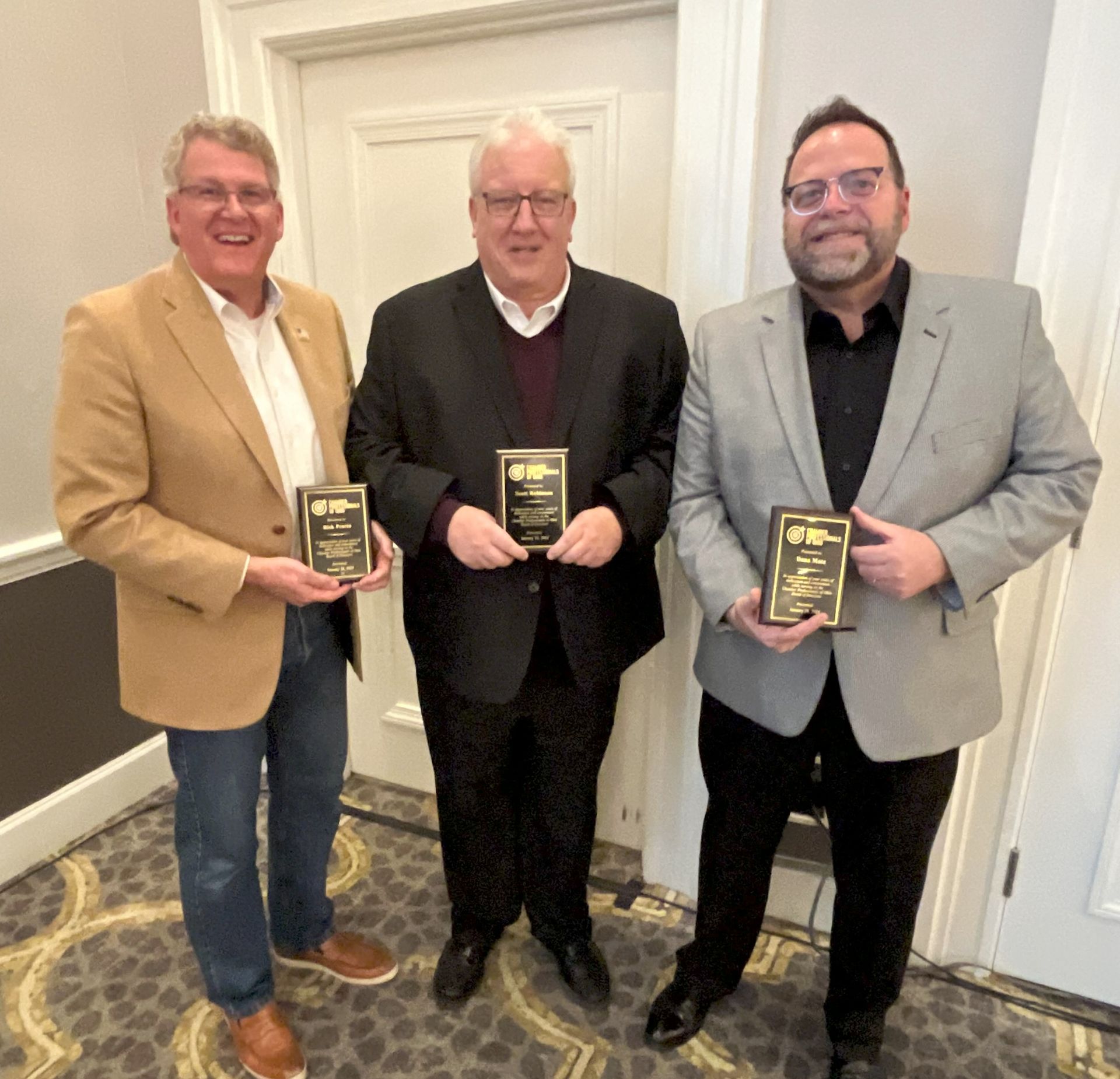 Three men standing next to each other holding awards