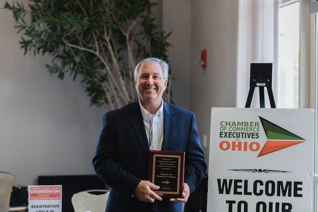 A man in a suit is holding a plaque in front of a welcome sign.