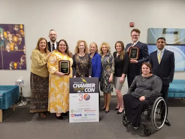 A group of people are posing for a picture in front of a sign that says chamber con.
