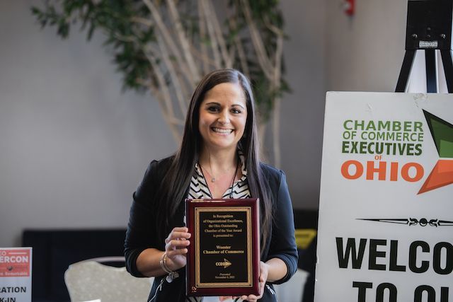 A woman is holding a plaque in front of a welcome sign.