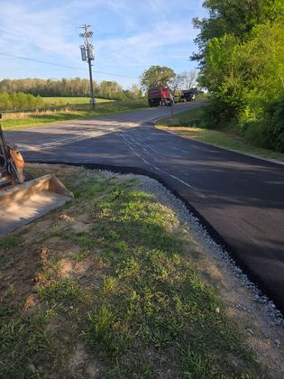 Damaged rural road with a large crack and a utility truck in the distance under a clear sky