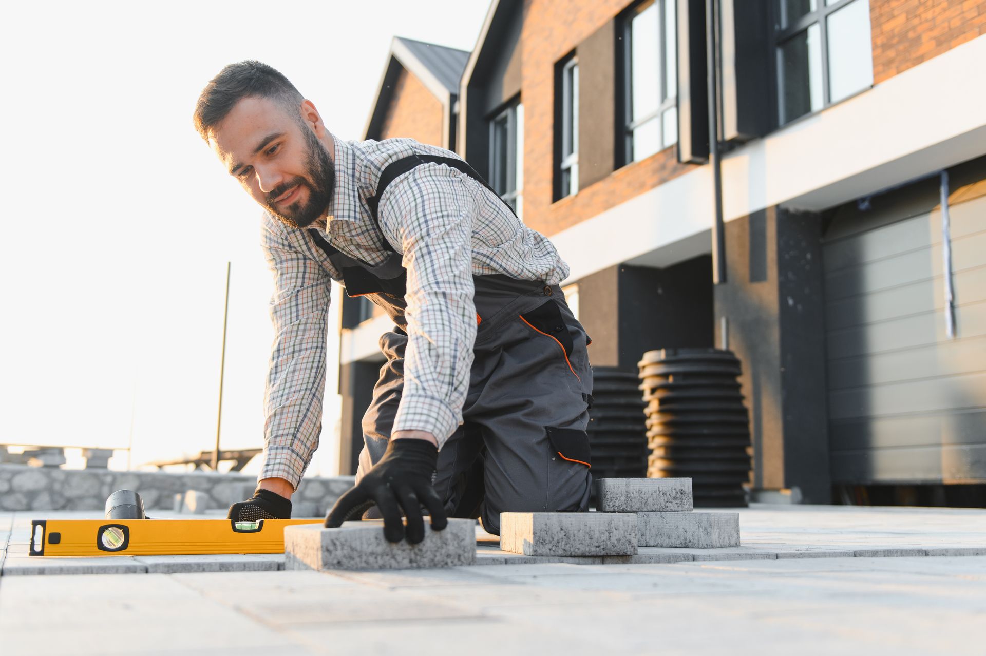 Worker installing paving stones and using a level outside a modern home.