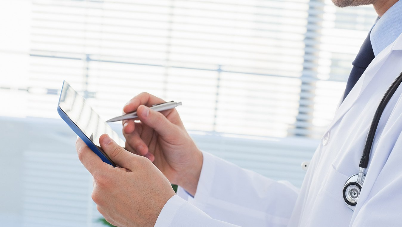 A doctor is writing on a clipboard with a pen.