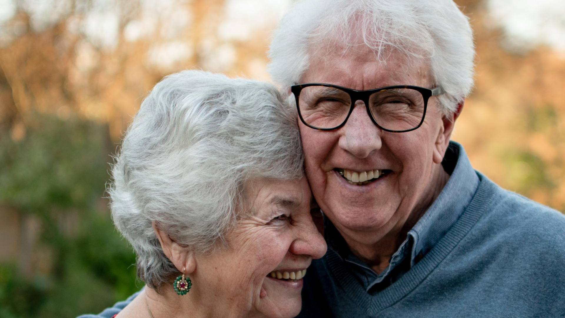 A man and a woman are smiling for the camera . the man is wearing glasses and the woman is wearing earrings.