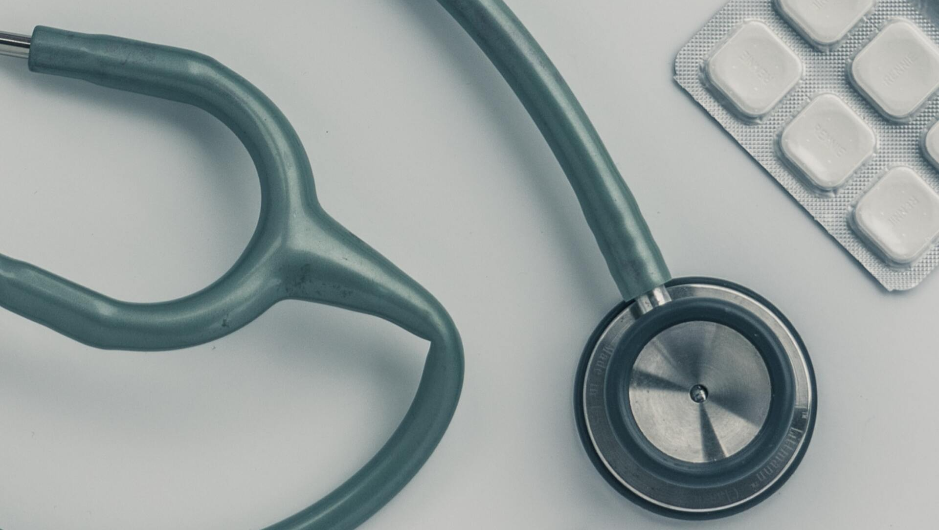 A stethoscope is sitting next to a blister pack of pills on a table.