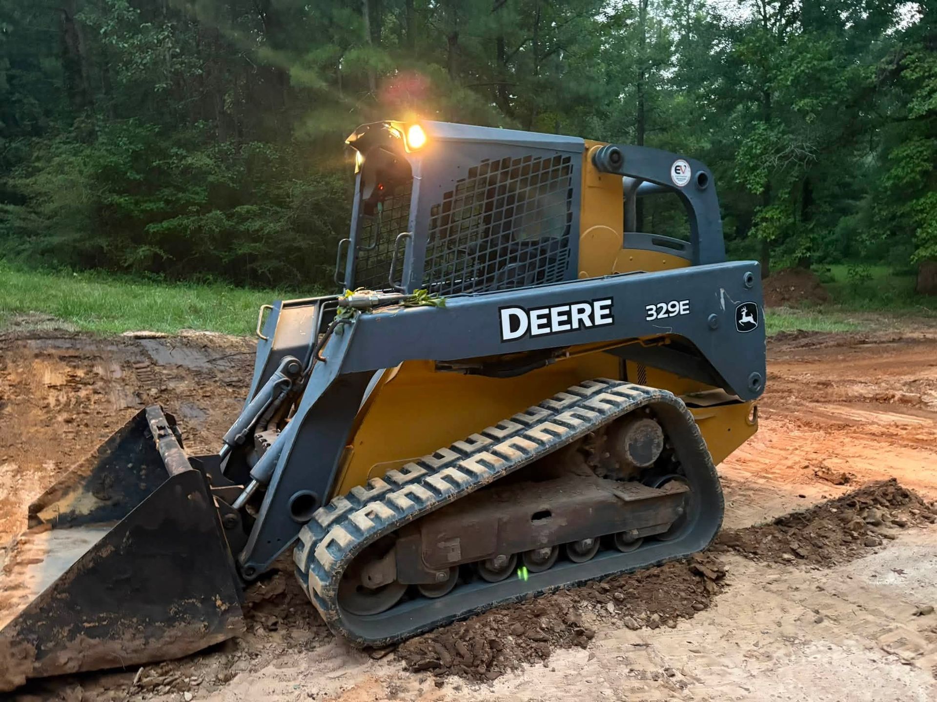 Black Deere skid-steer loader with bucket on a dirt path in a wooded area