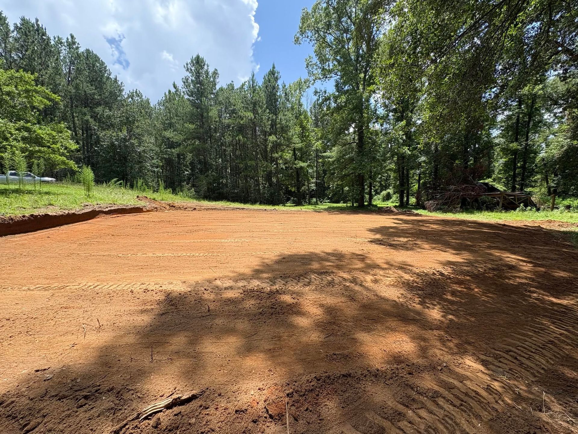 Dirt clearing surrounded by green trees under a bright blue sky