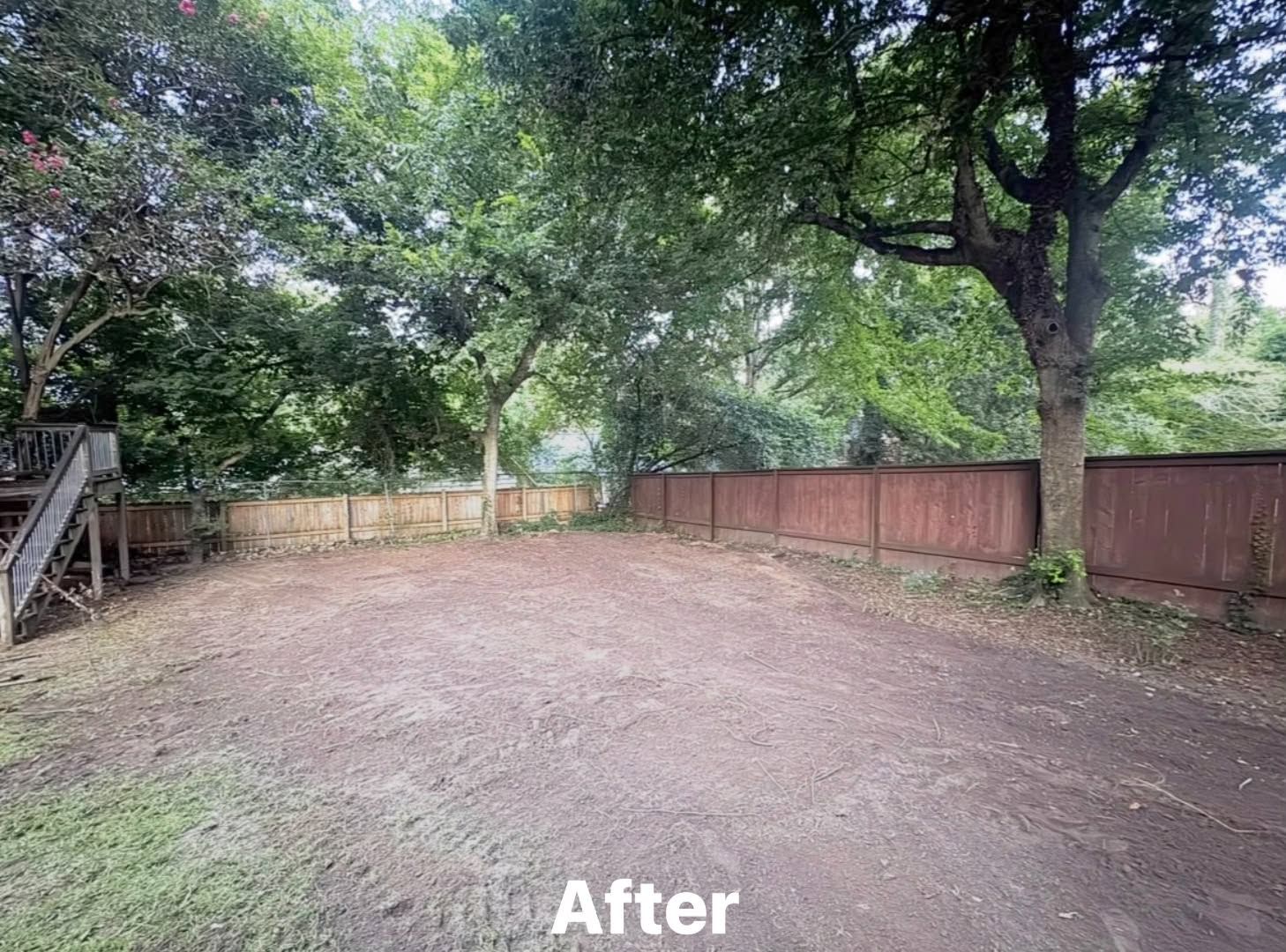Empty gravel yard bordered by trees and a wooden fence, with a staircase at left.