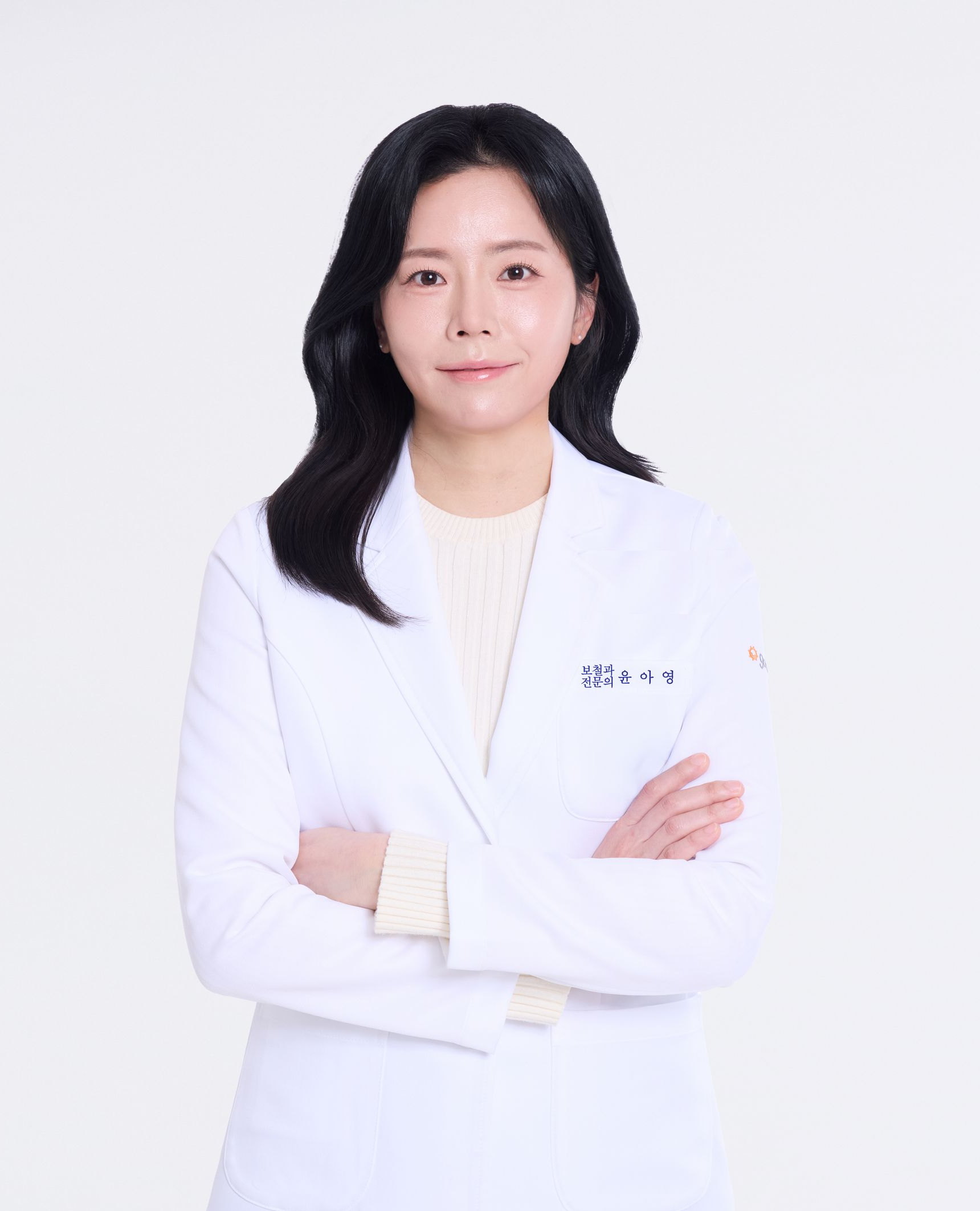 A smiling woman in dark blue scrubs with arms crossed, possibly a medical professional. Plain, neutral background.