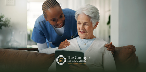 An assisted living staff member happily talking with a senior using a tablet sitting on a couch