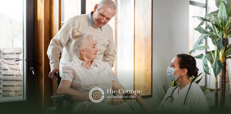 A man pushing his elderly wife in a wheelchair while a respite caregiver is talking to her