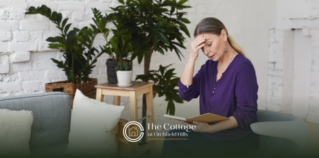 A caregiver sitting on a couch looking a her notes with her hand on her forehead; looking exhausted.