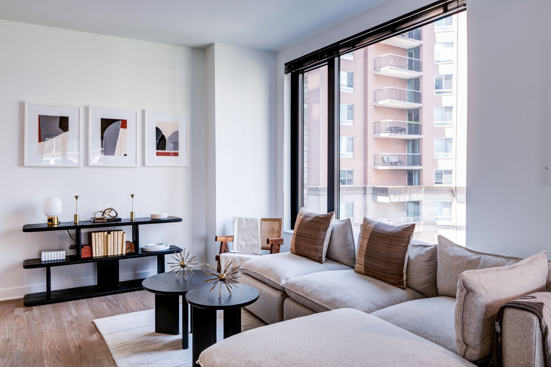 Modern living room with beige sectional, black coffee table, framed wall art, and large city-view windows  at  Solaire 7607 Old Georgetown in Bethesda, MD