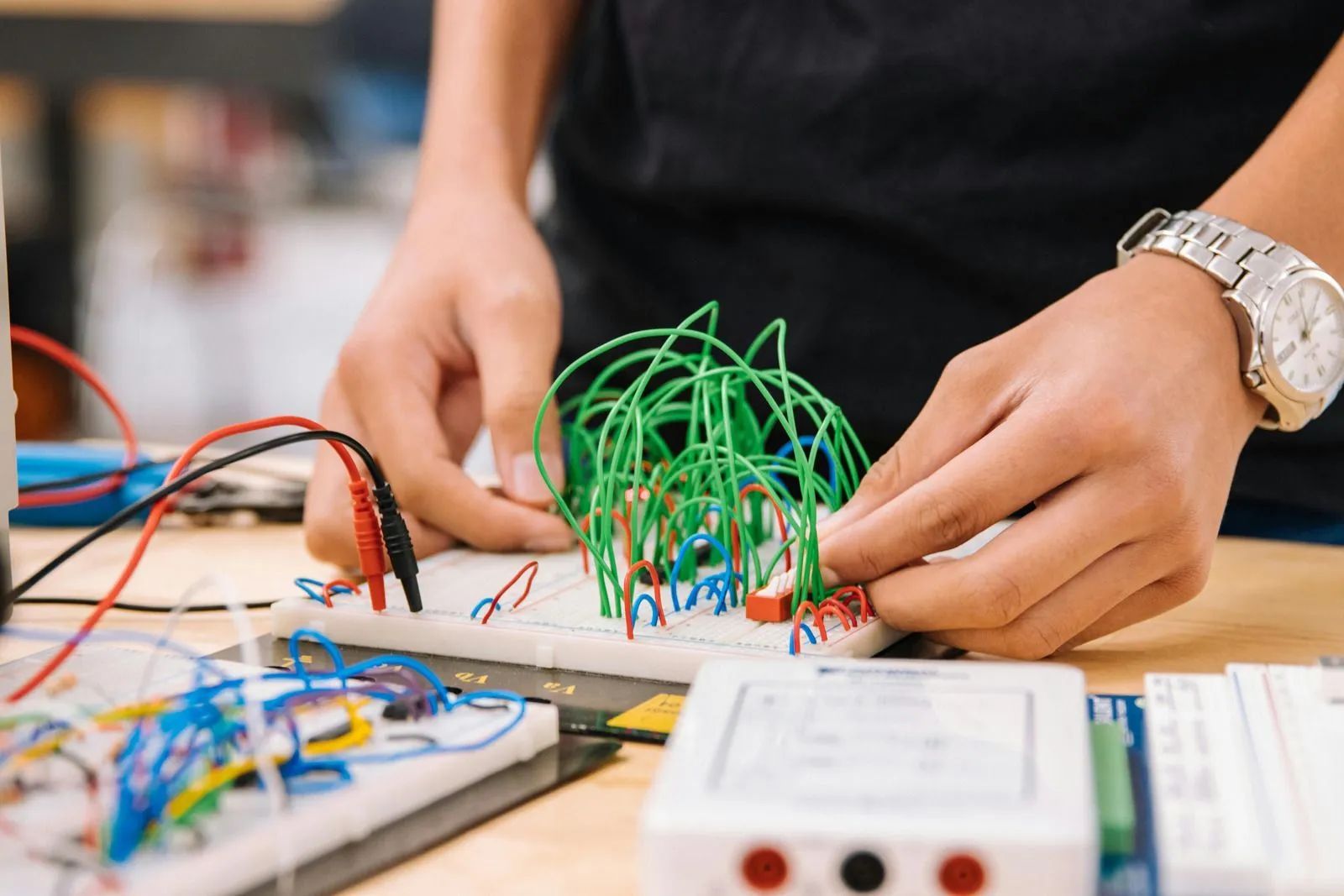 Hands assembling a green wire sculpture on an electronics workbench with circuit boards and tools