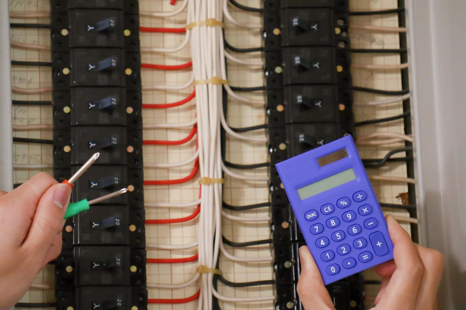 Person holding wires and calculator in front of an open electrical panel.