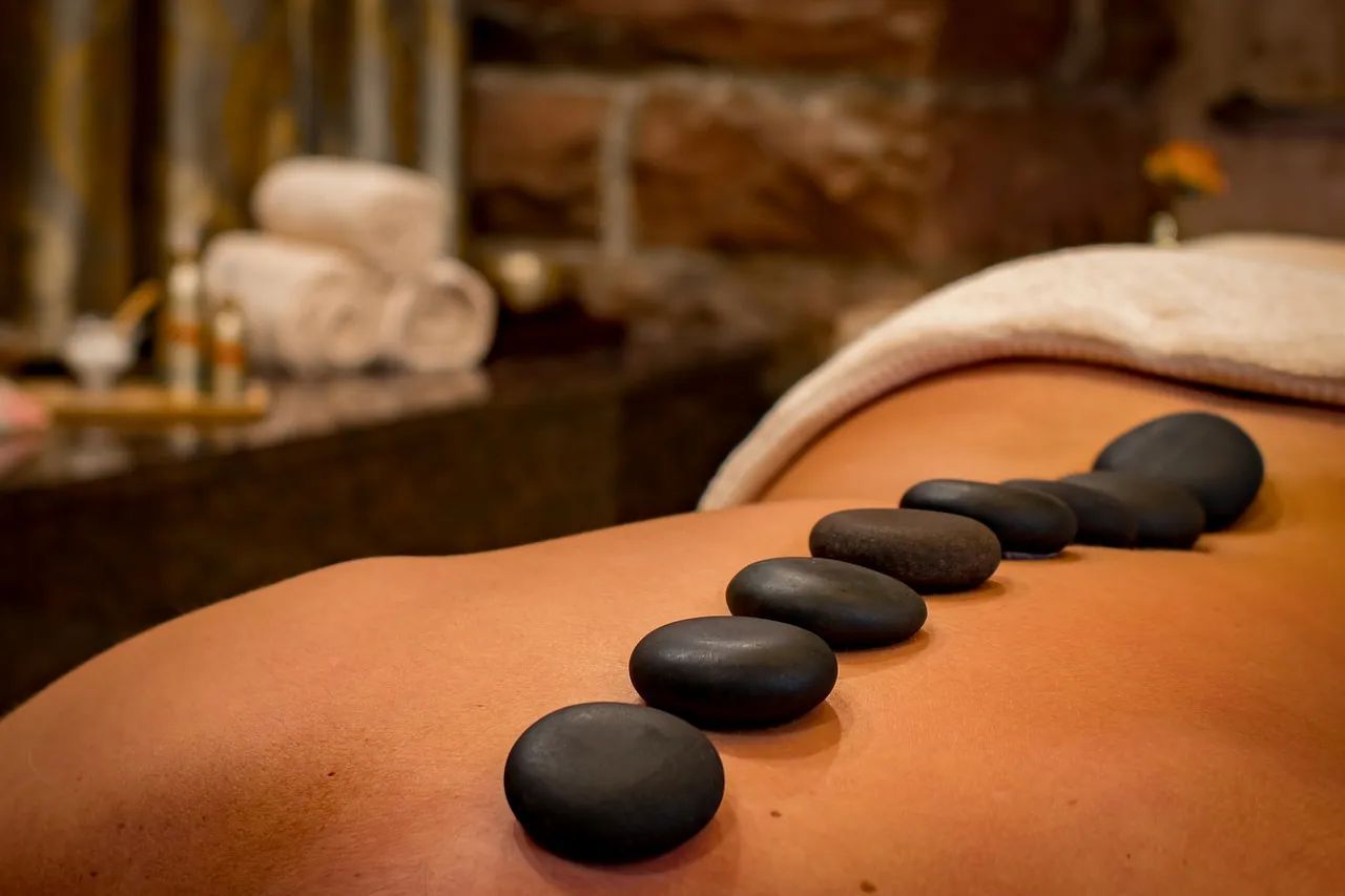 A row of smooth, dark, hot stones resting along a person's back during a massage in a spa setting.