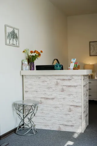 A rustic white wood reception desk with a floral vase, situated next to a decorative metal side table in a waiting area.