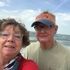 Couple smiling on a windy beach, ocean waves behind them and one wearing a Florida cap