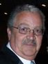 Close-up portrait of a man with glasses and a mustache in a dark suit, against a dark background